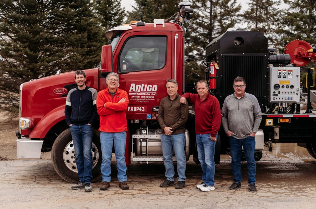 Mark Reimer, Matt Shinners, Chris Shinners, David West and Jason Jansen stand in front of a red Antigo Construction truck.