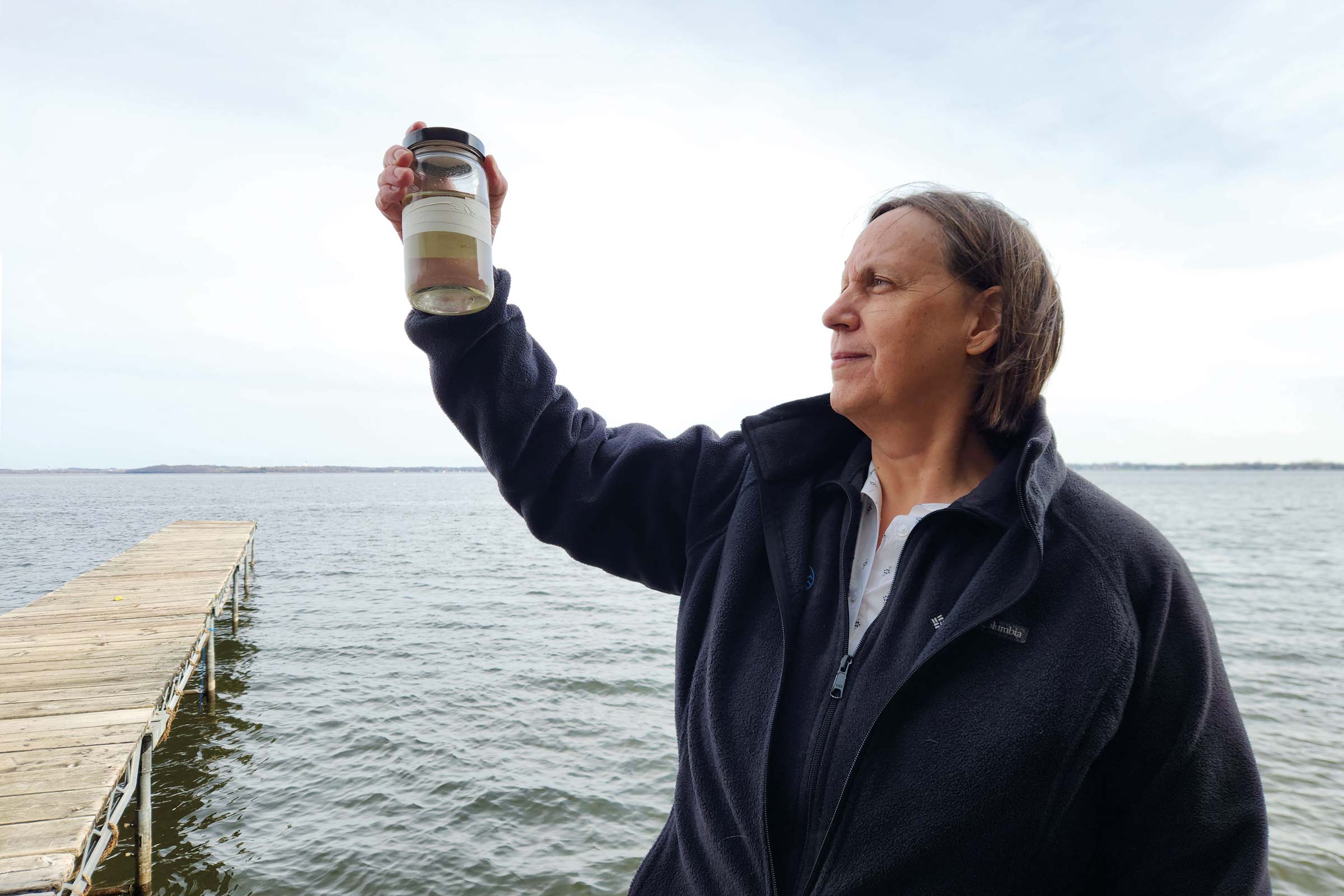 Emily Stanley holds up a water sample while standing in front of Lake Mendota